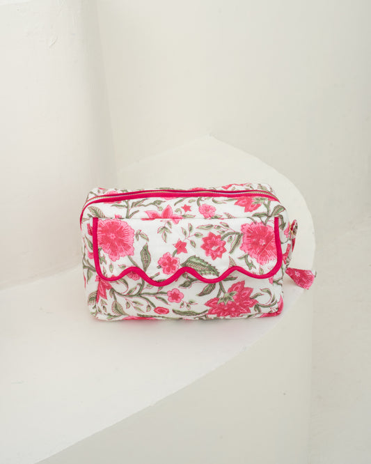 A rectangular cosmetic pouch with a pink and green floral print on a white background, featuring a scalloped pink trim and a small tassel zipper pull, set against a plain white background.