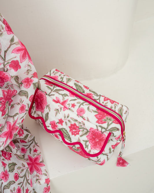A small rectangular zip pouch with a pink and green floral print on a white background, accented with bright pink trim and a matching tassel zipper pull, shown next to a matching floral fabric piece on a white surface.