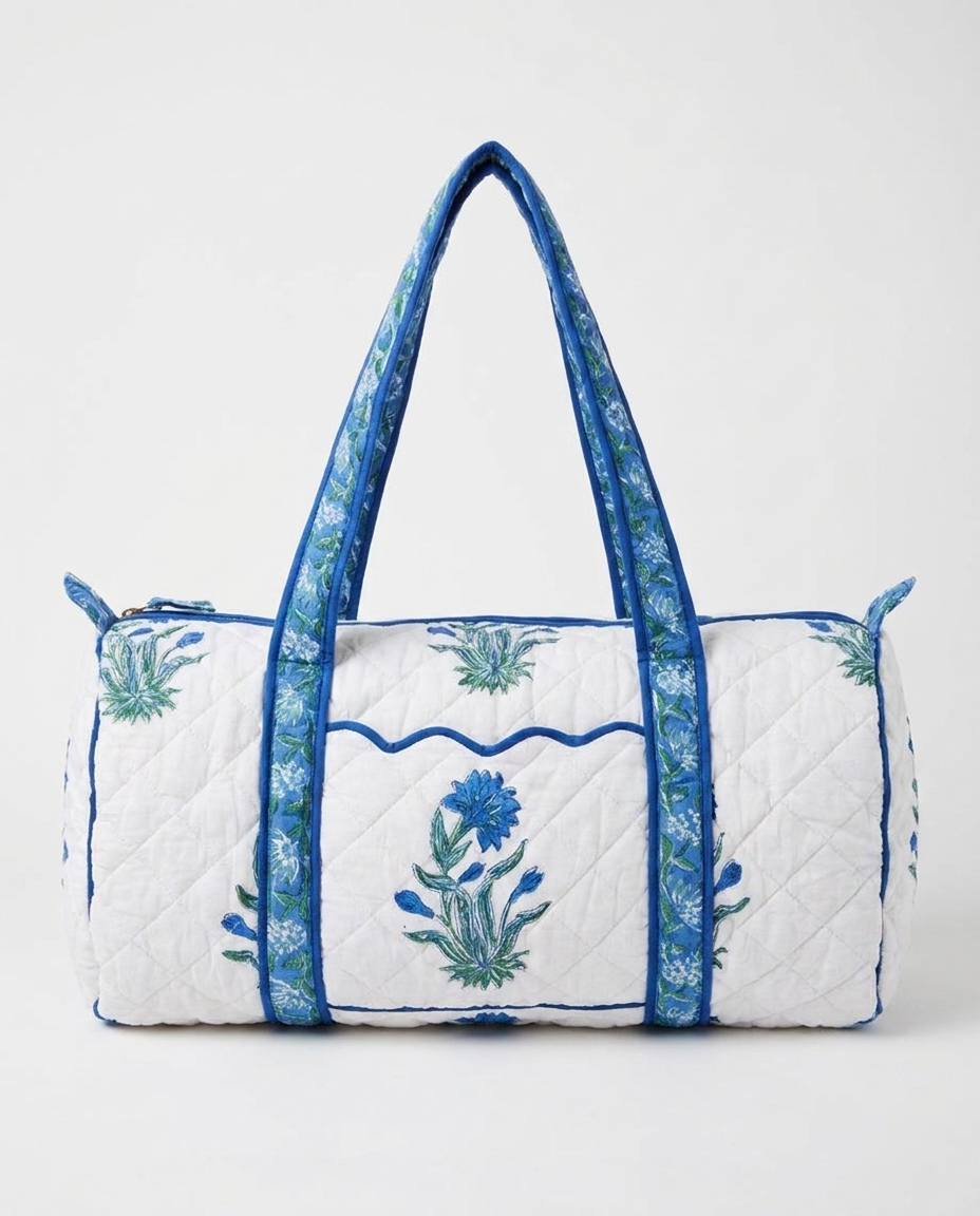 A quilted duffle bag with a white body, blue floral motifs, and blue patterned handles, shown against a plain light gray background.